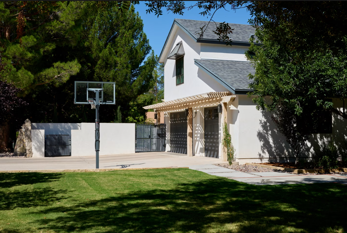 White house with basketball hoop on a grassy lawn; trees surround the property.
