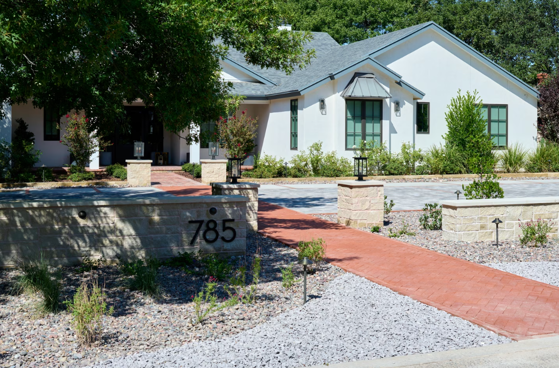 White stucco house with red brick walkway and low stone wall marked