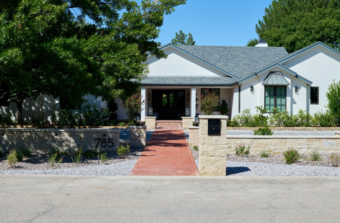White house with gray roof, red brick pathway, and stone retaining walls.