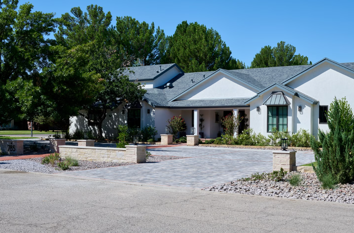 White house with gray roof and circular paved driveway, under a clear blue sky.