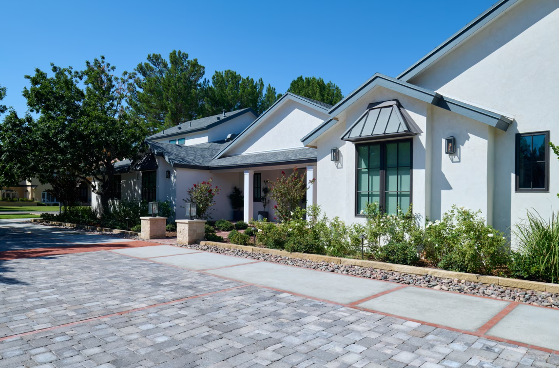 White stucco house with blue roof, green window, and stone driveway under a clear, blue sky.