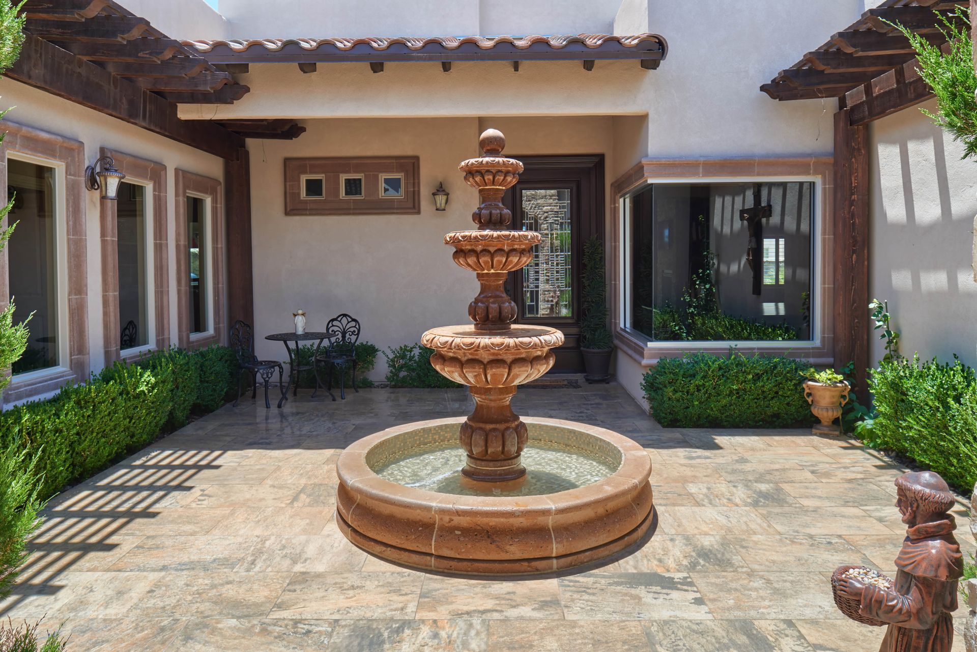 Courtyard with a three-tiered fountain. Beige walls, stone patio, plants, and a small table.
