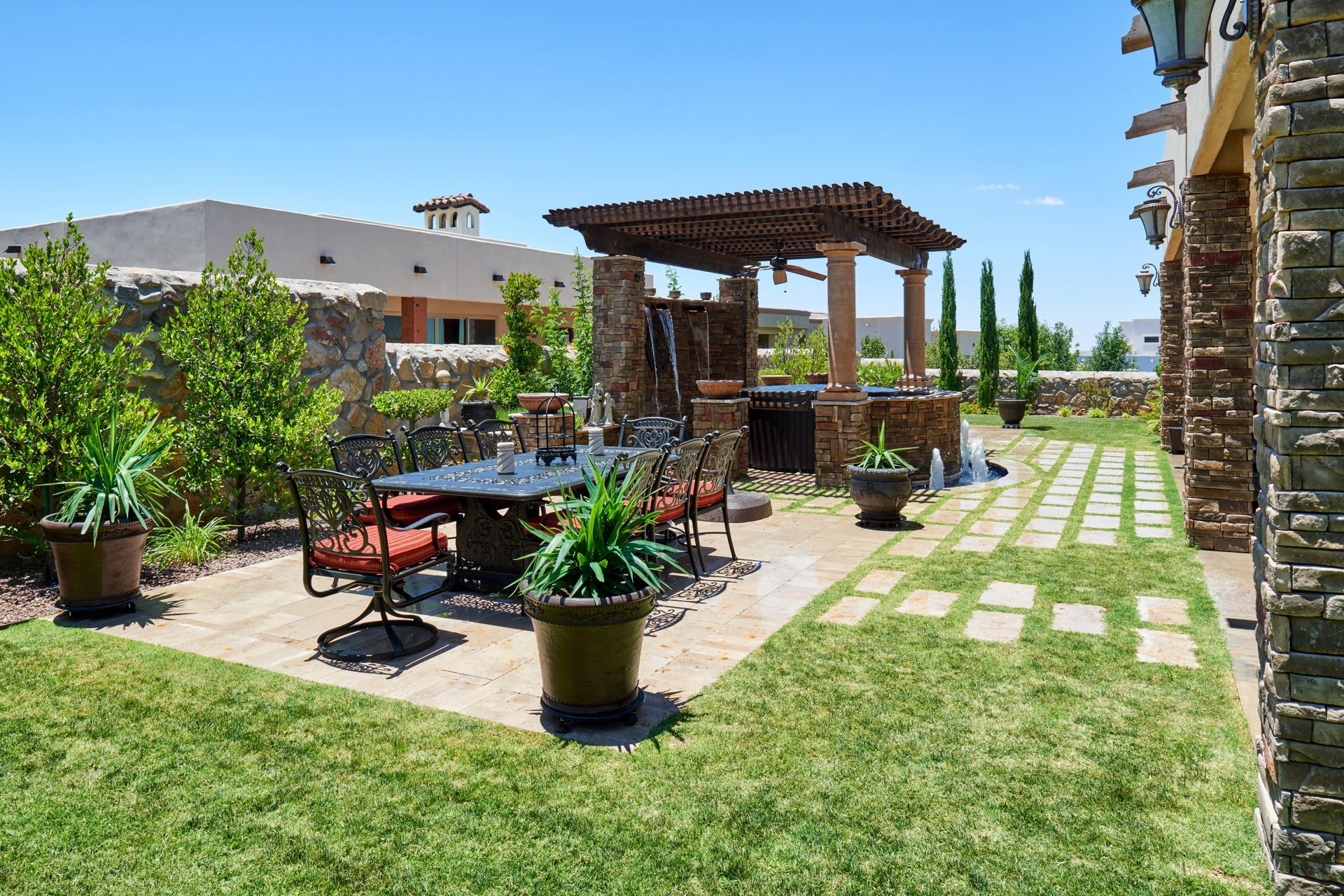 Patio with dining table, pergola, water feature, and potted plants on a sunny day.