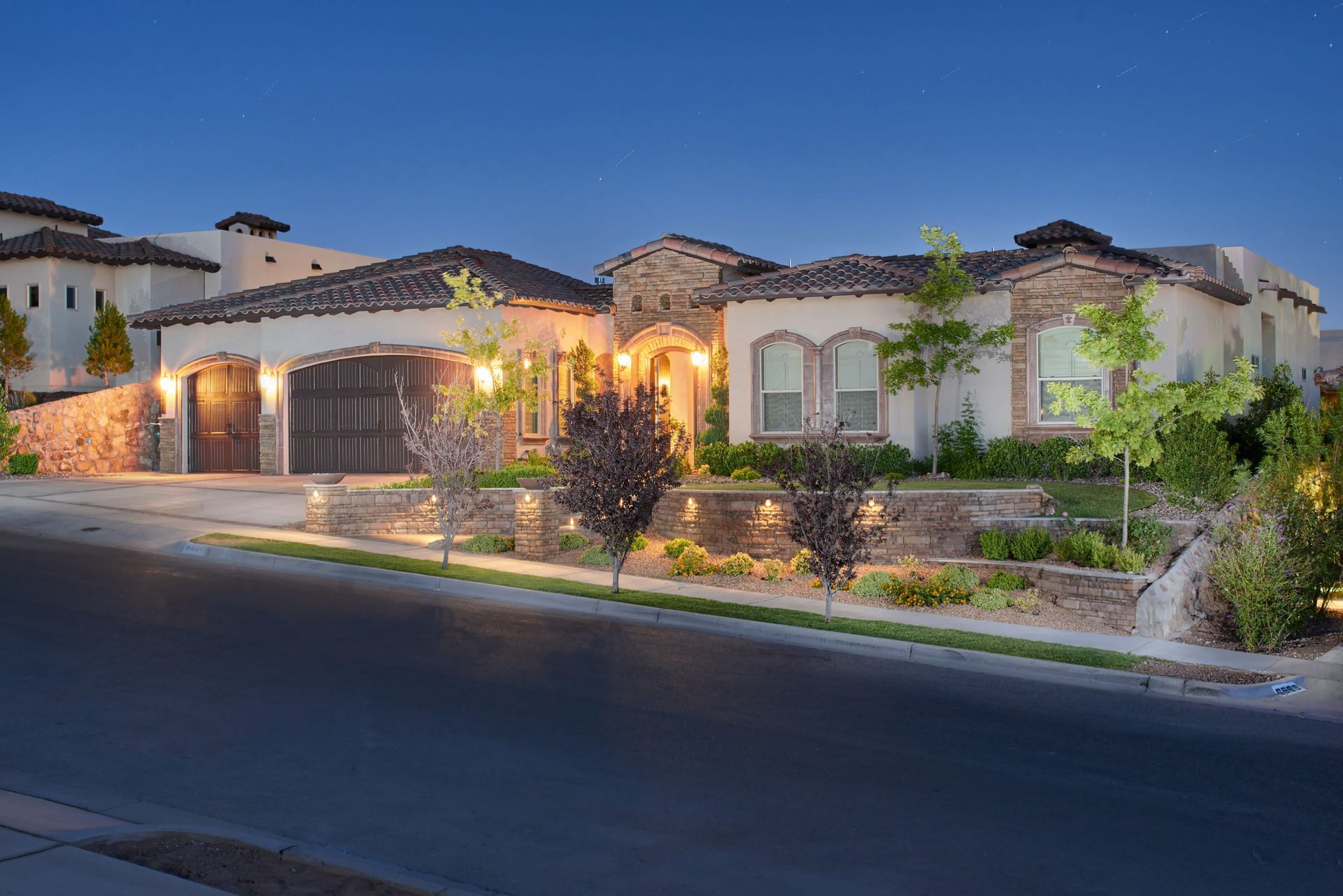 Elegant two-story house at dusk, with garage, landscaping, and lit pathway.