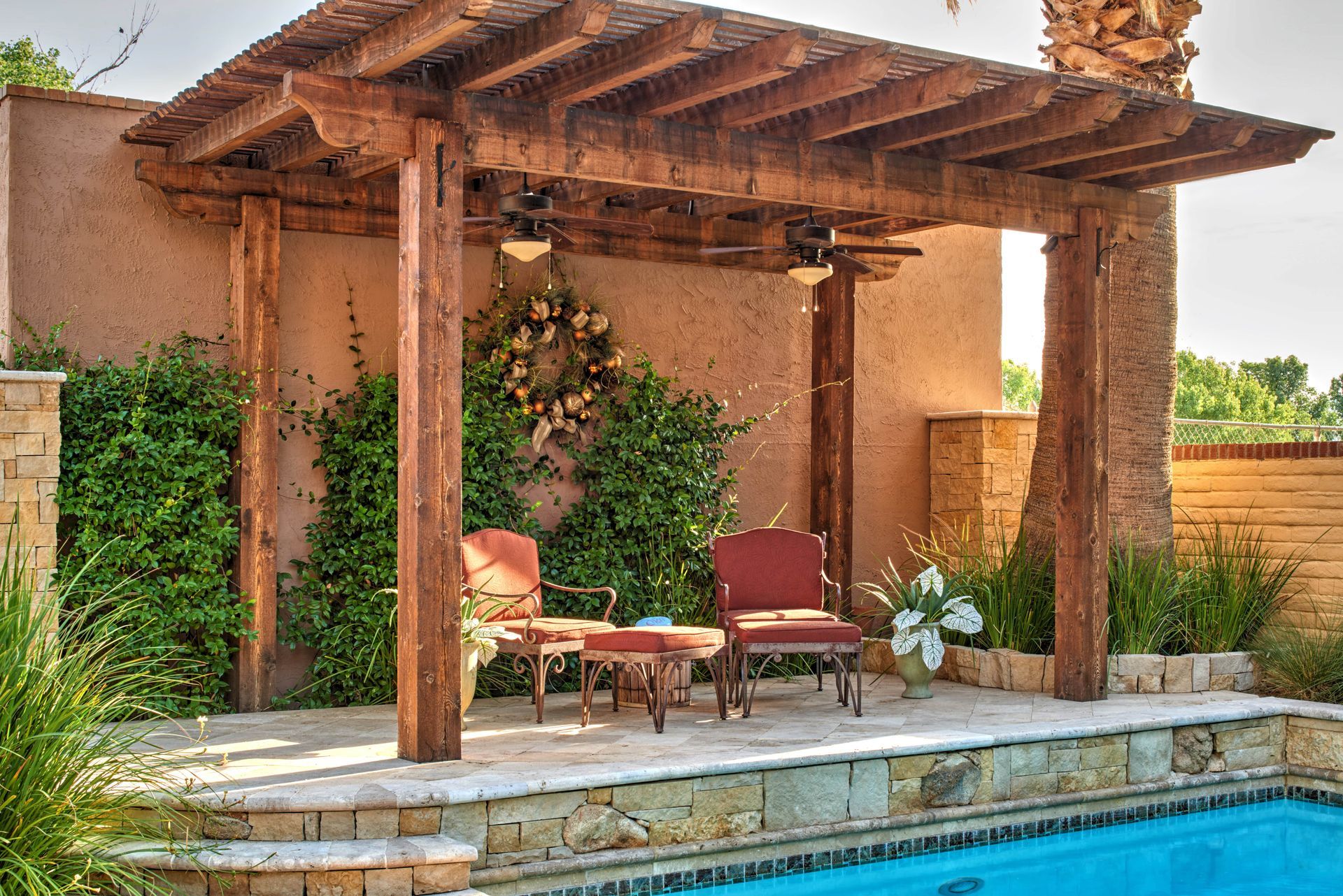 Wooden pergola over a patio with two chairs by a pool.
