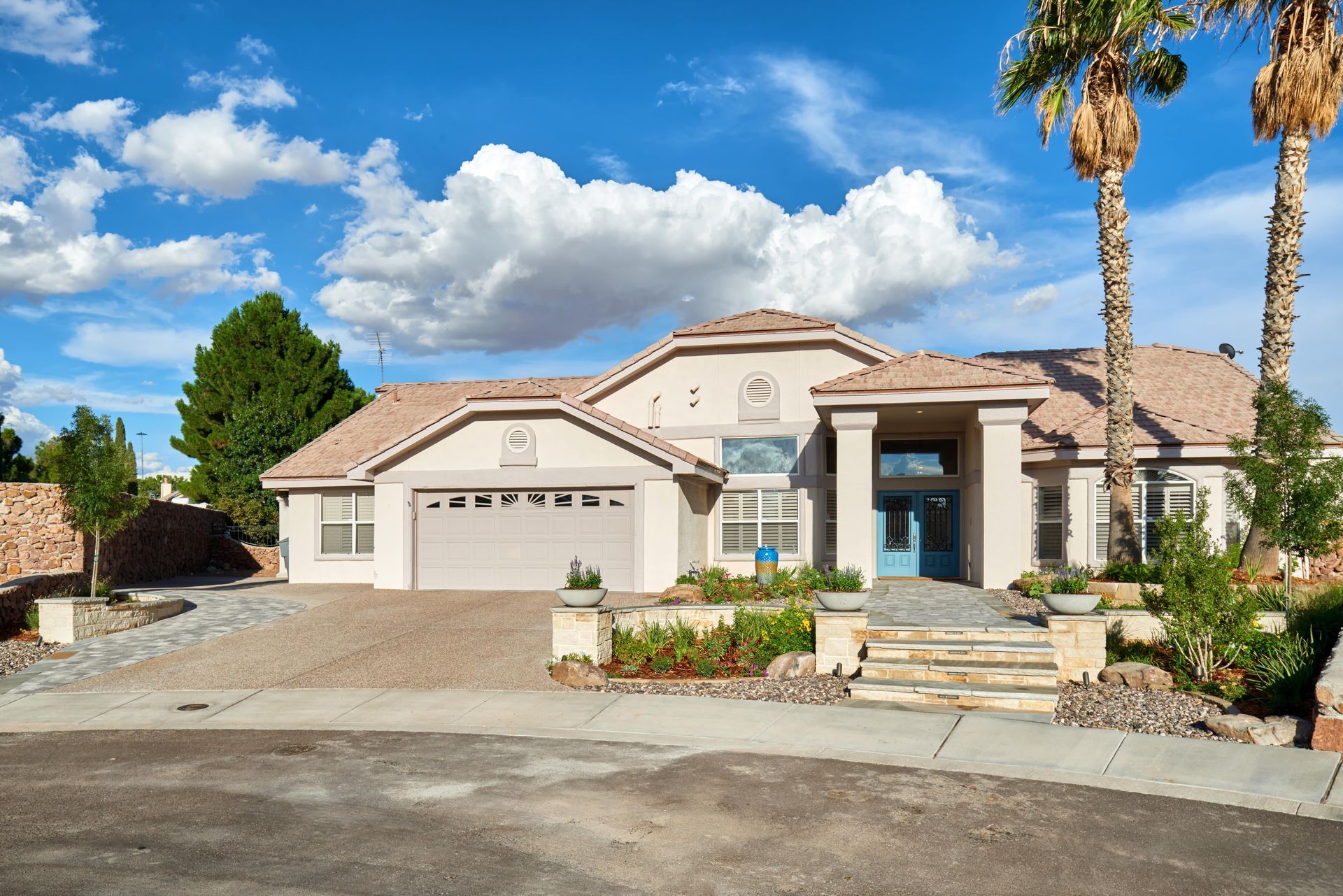 Beige house with a blue front door, palm trees, and a cloudy sky.