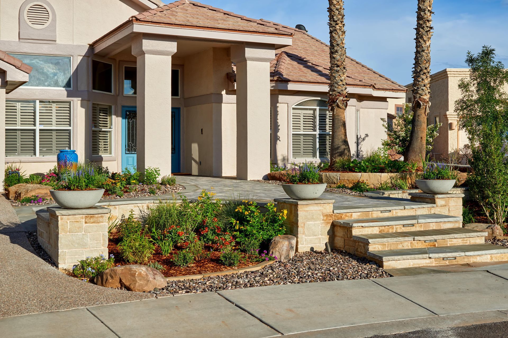 Beige house entrance with stone steps, columns, potted plants, and blue front door.