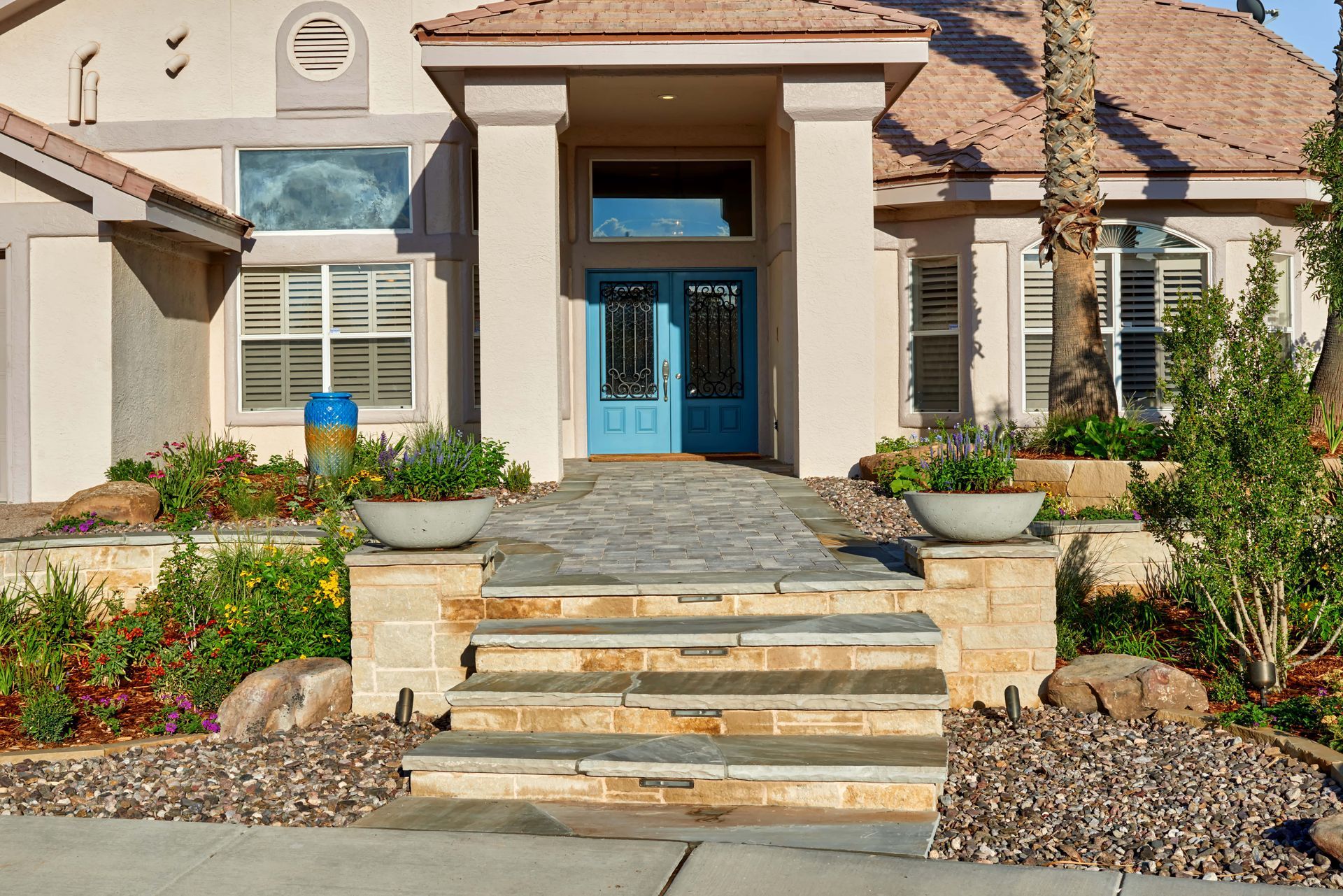 Beige house with blue front door, stone steps, and planters filled with greenery.