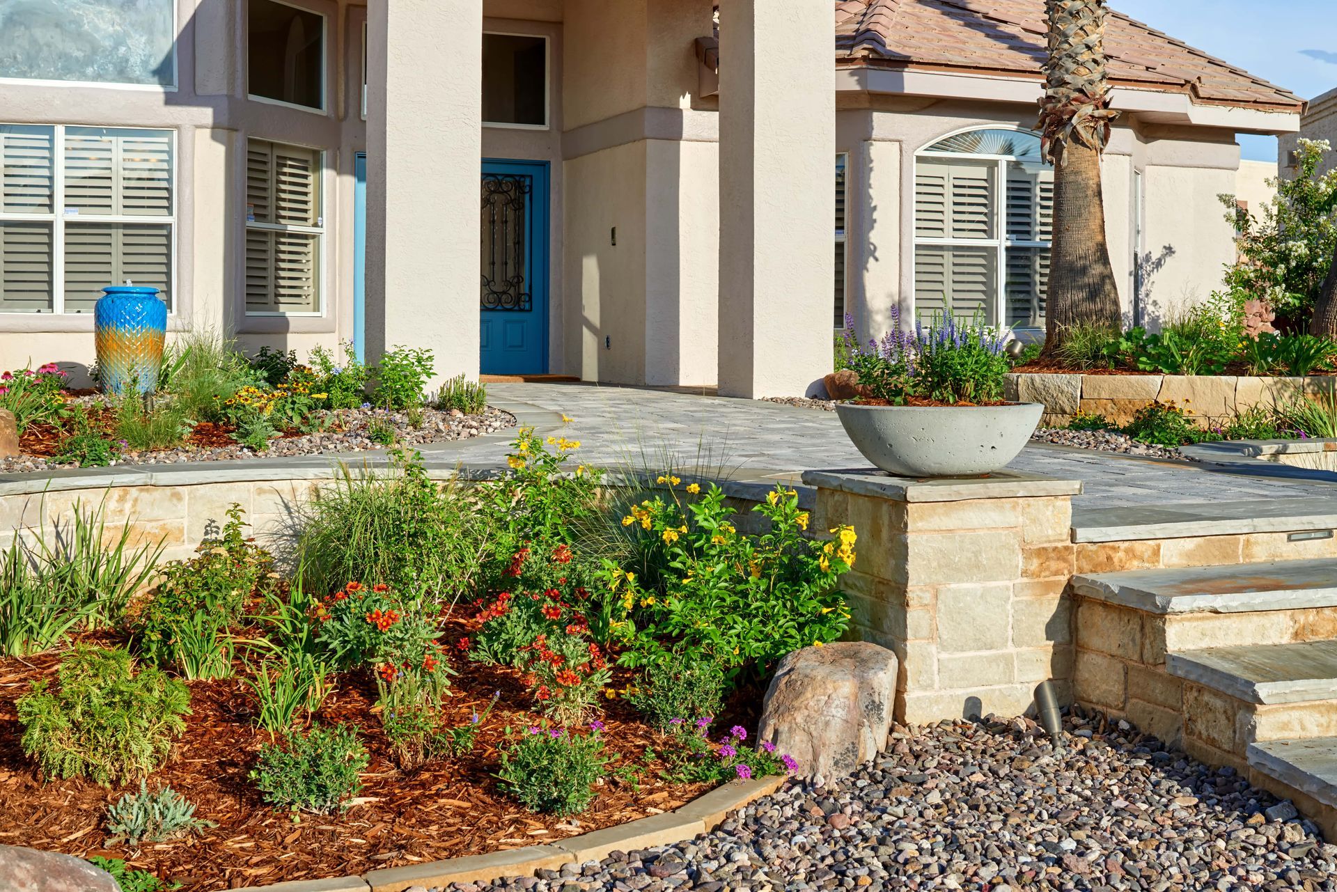 A landscaped yard with a concrete flower bowl, leading up to a beige house with blue door.