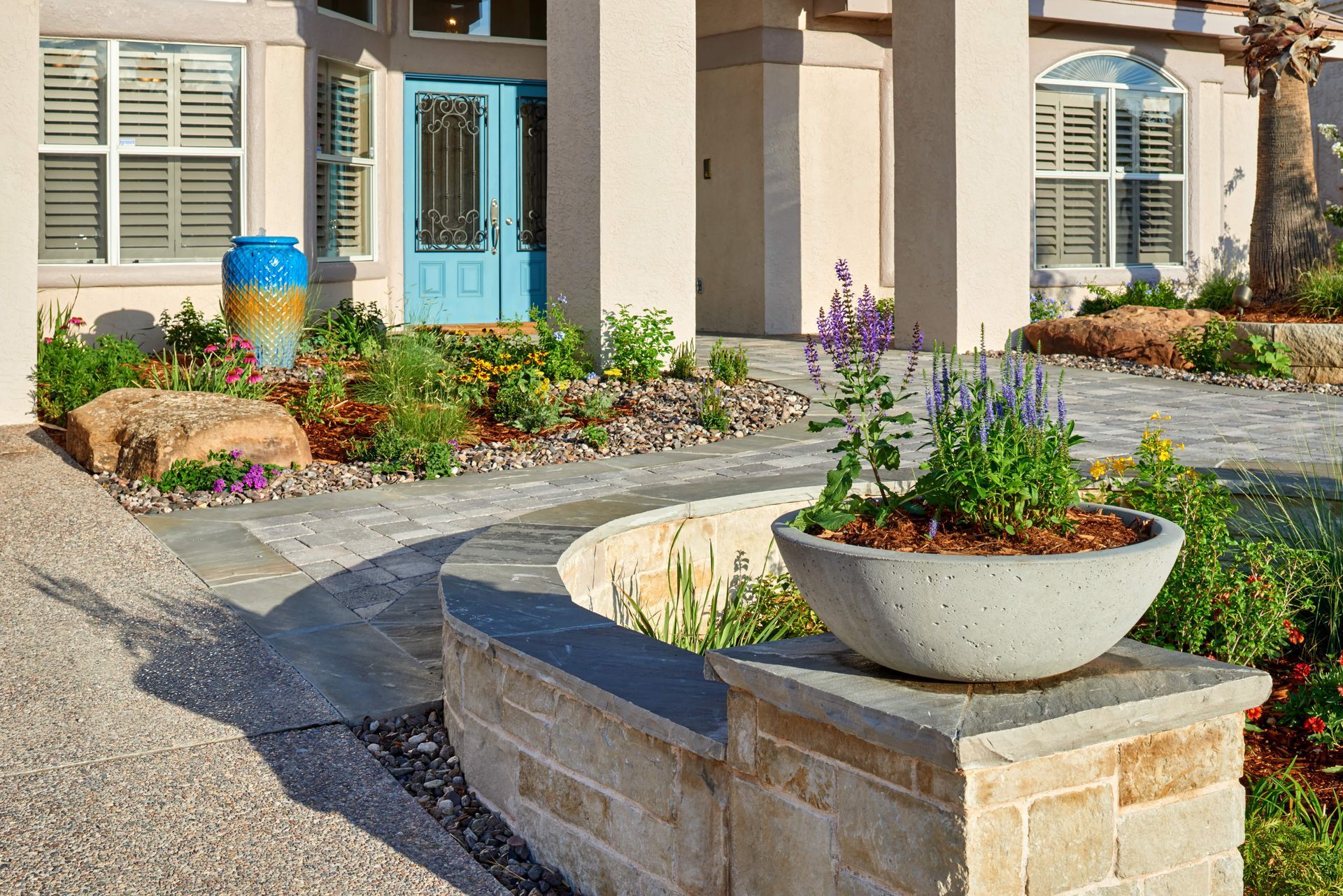 Exterior of a house with a blue door, lush landscaping, and a curved stone wall.