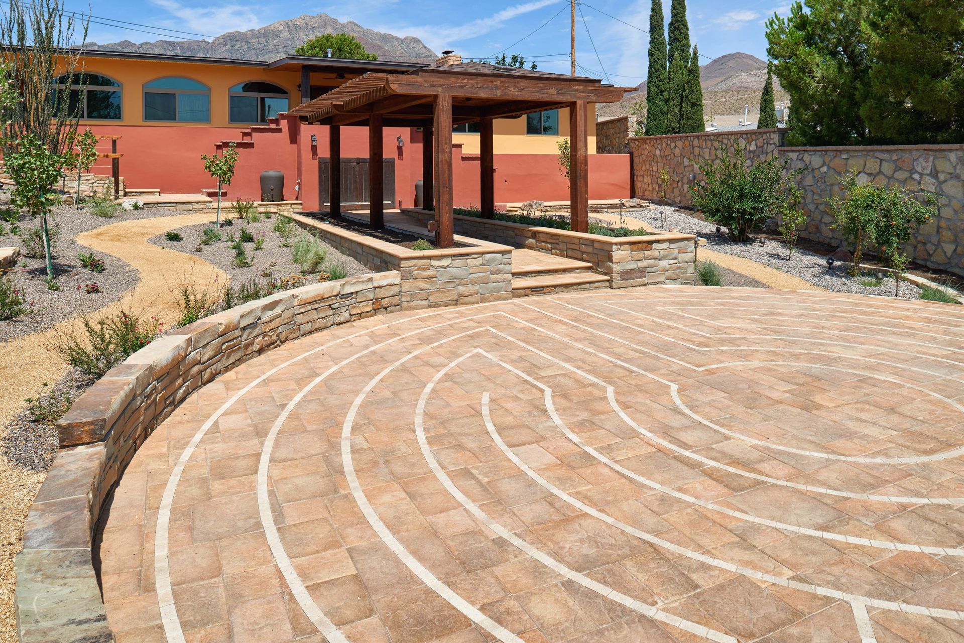 Brick labyrinth path leading to a wooden pergola in a desert landscape.
