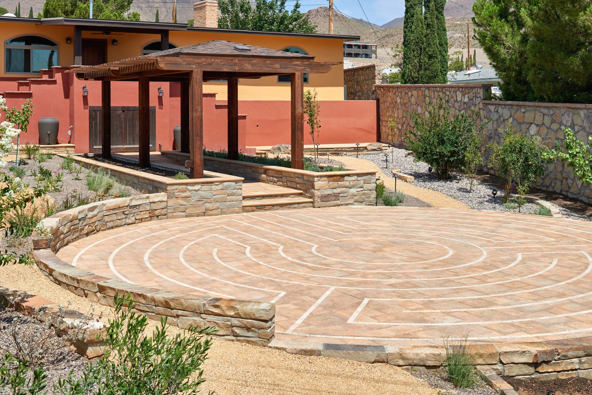 Circular stone labyrinth with wooden pergola in a landscaped outdoor setting.