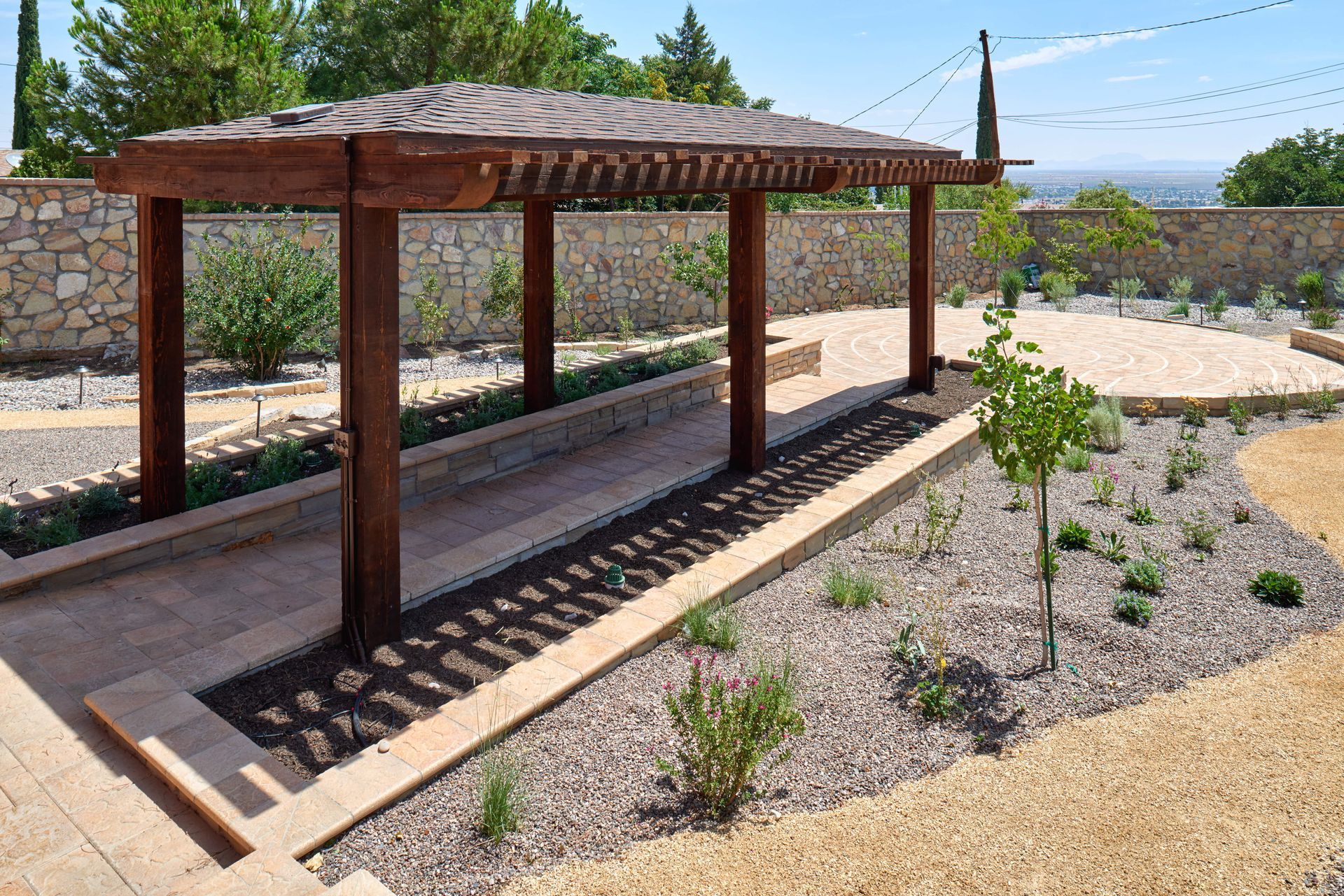 Wooden pergola in a landscaped garden with gravel, plants, and a stone wall.
