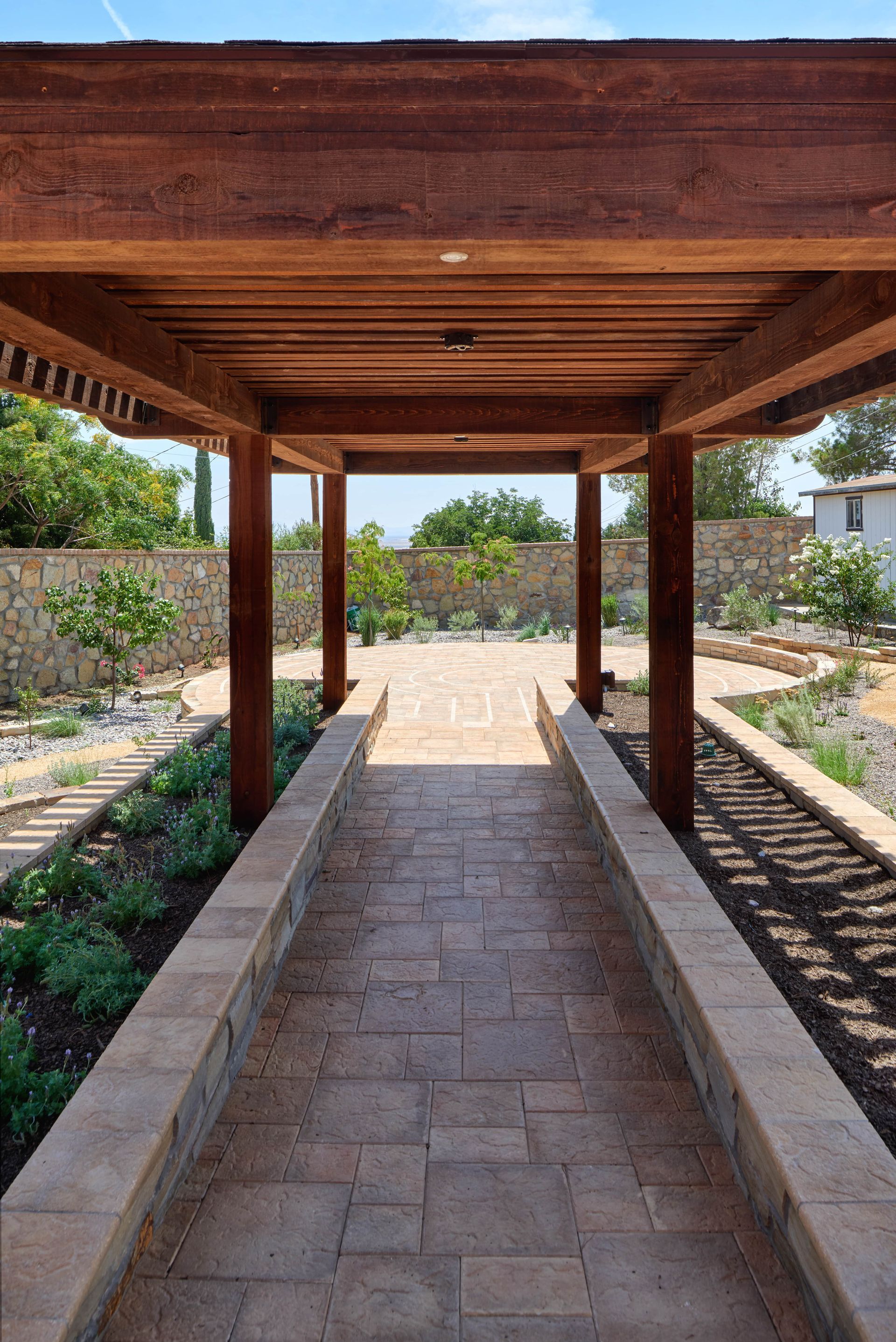 Wooden pergola walkway leading to a garden with stone pathways and greenery.