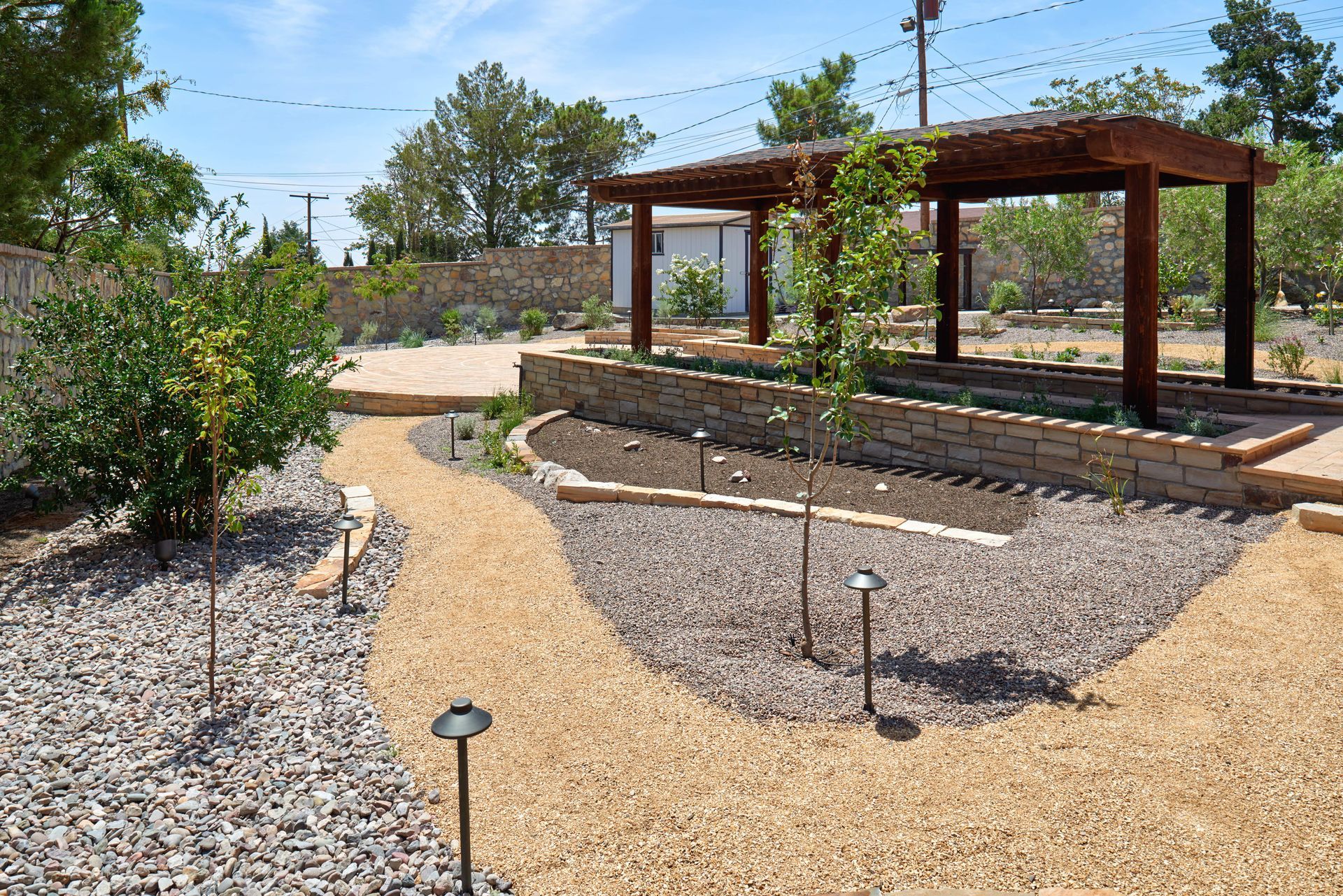 Gravel pathways lead through a desert garden with a wooden pergola.
