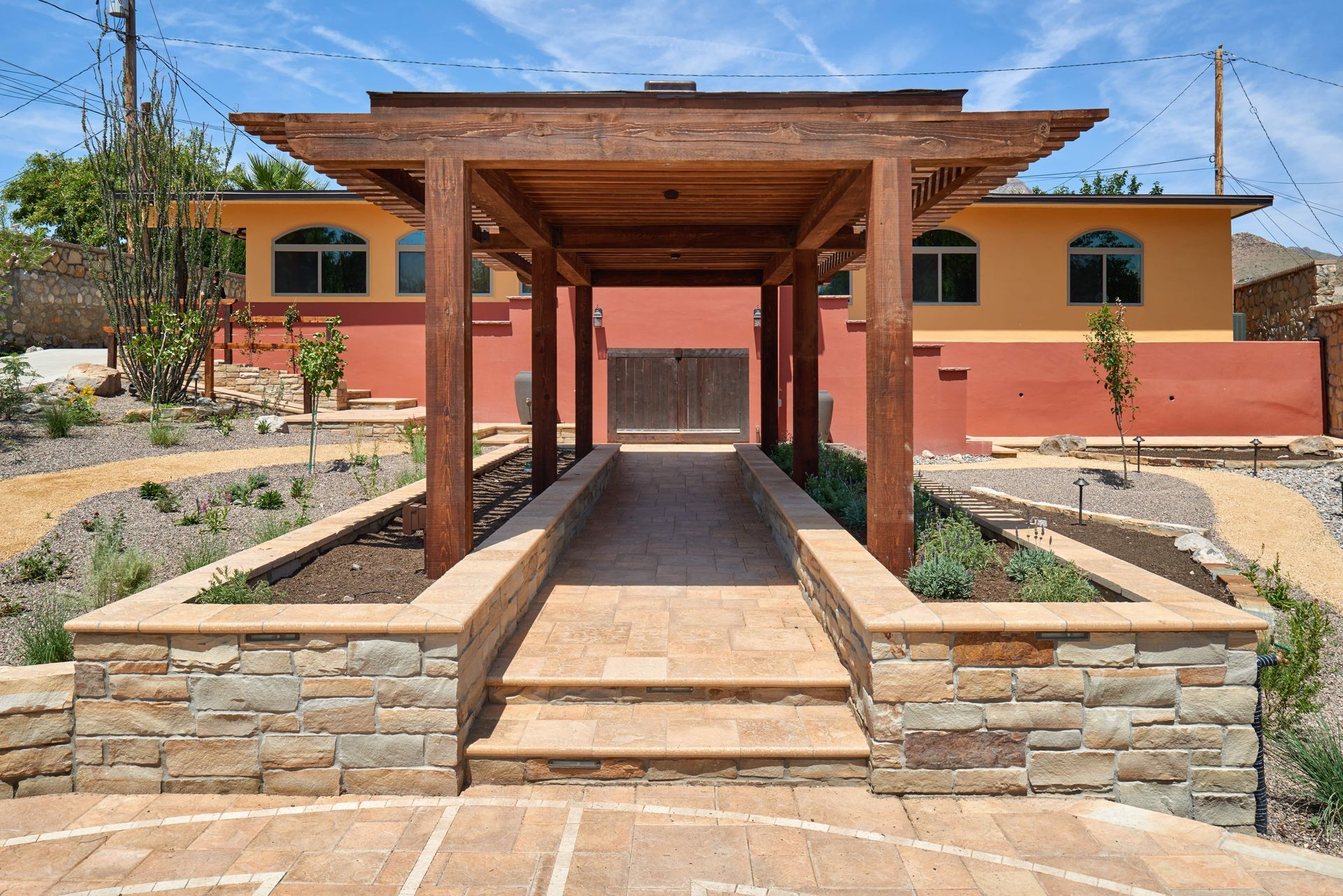 Wooden pergola over a stone path leading to a building with an orange and red exterior.