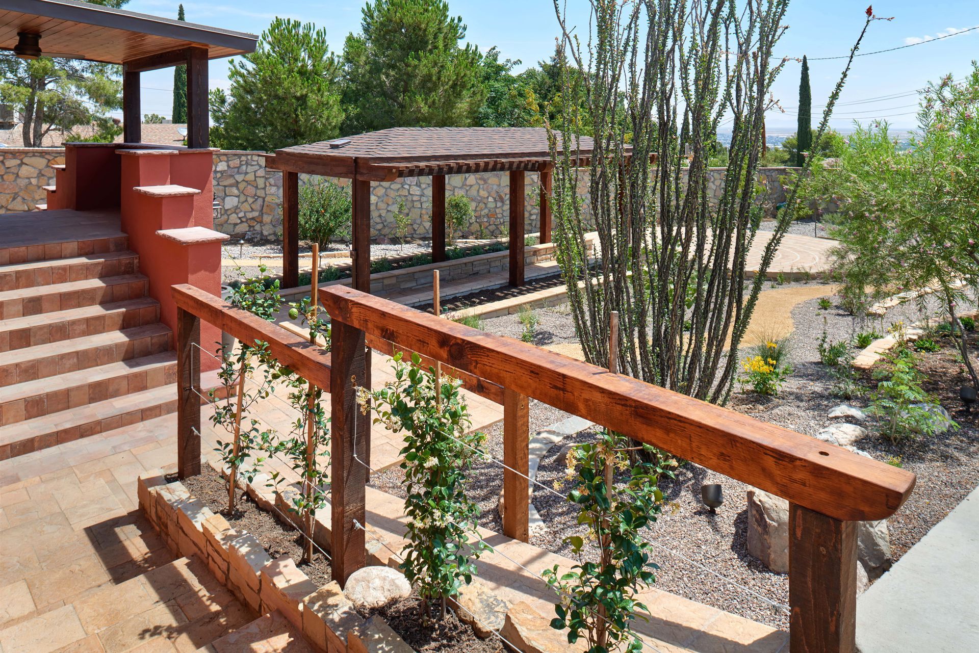 Wooden deck with handrail, steps leading up, and a pergola in a landscaped yard.