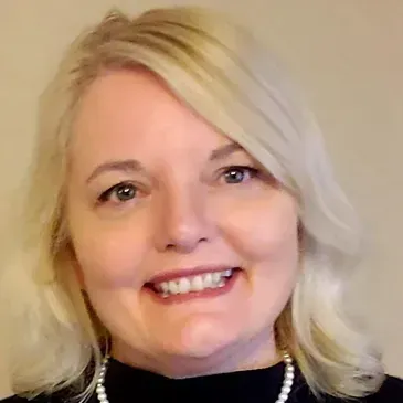 A woman with blonde hair and a pearl necklace is smiling for the camera.