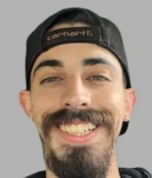 A man with a beard is wearing a carhartt hat and smiling.