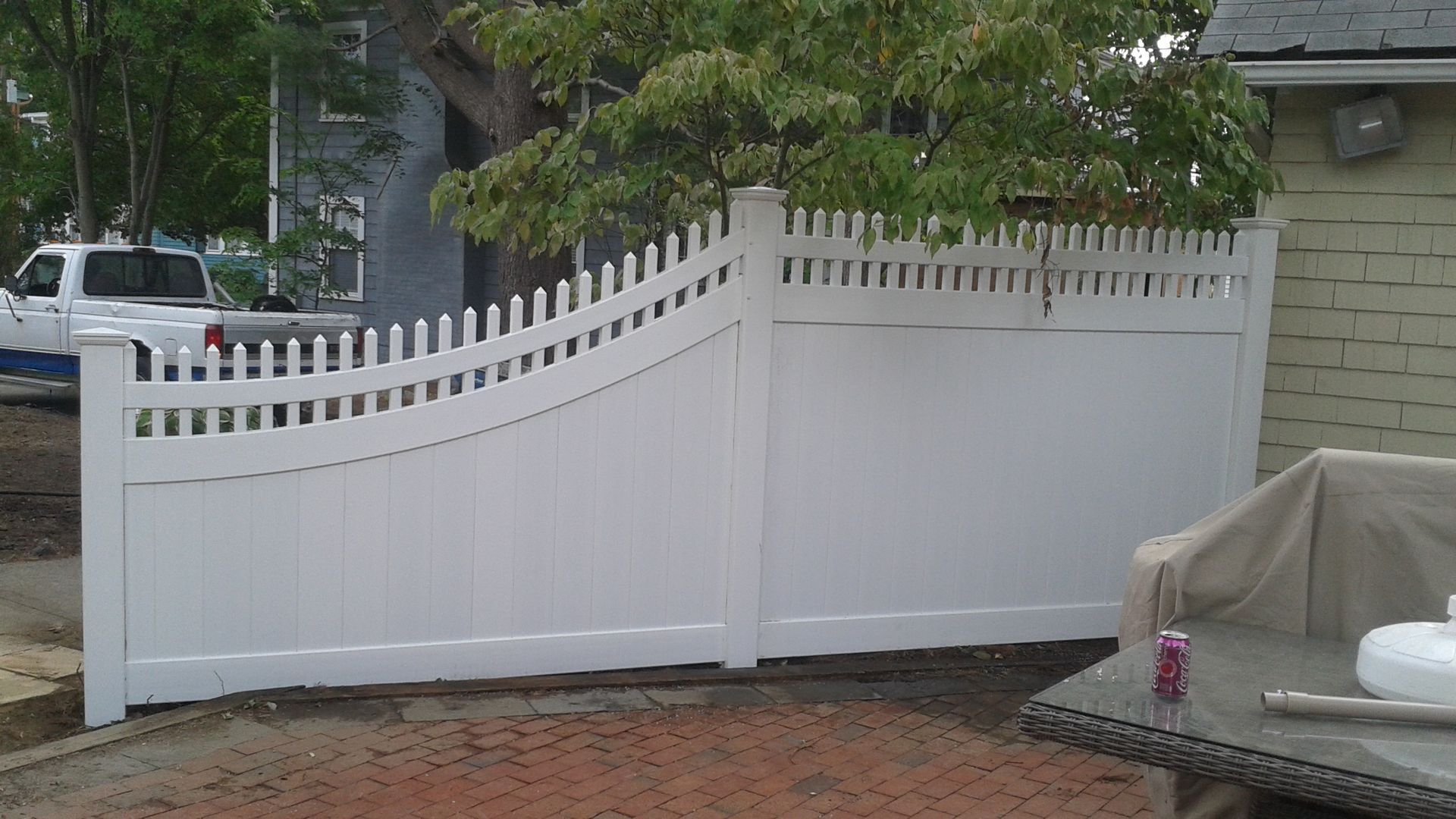 White picket fence with arched design and gate in front of a building.