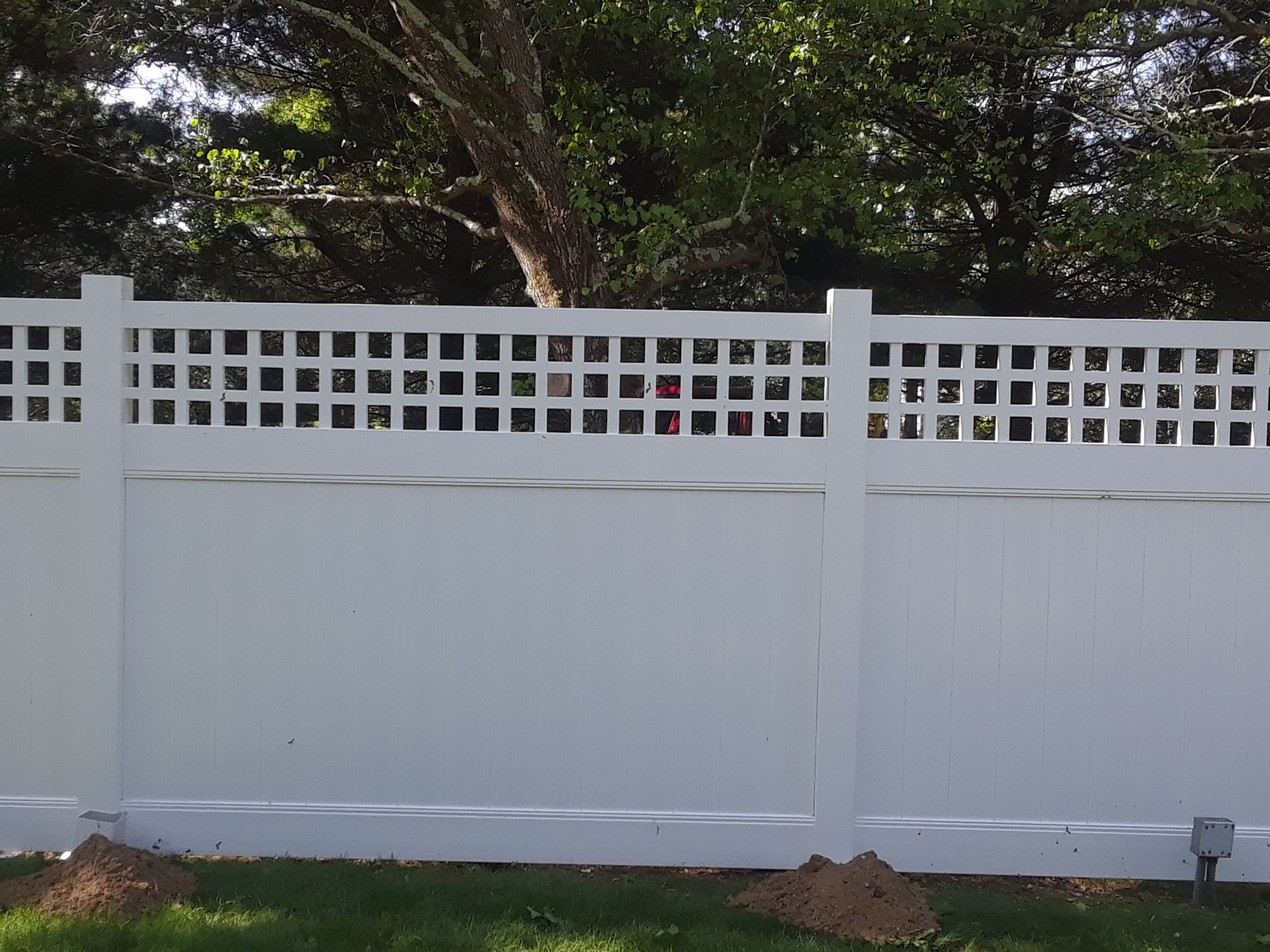 White vinyl fence with lattice top in front of green grass and trees.