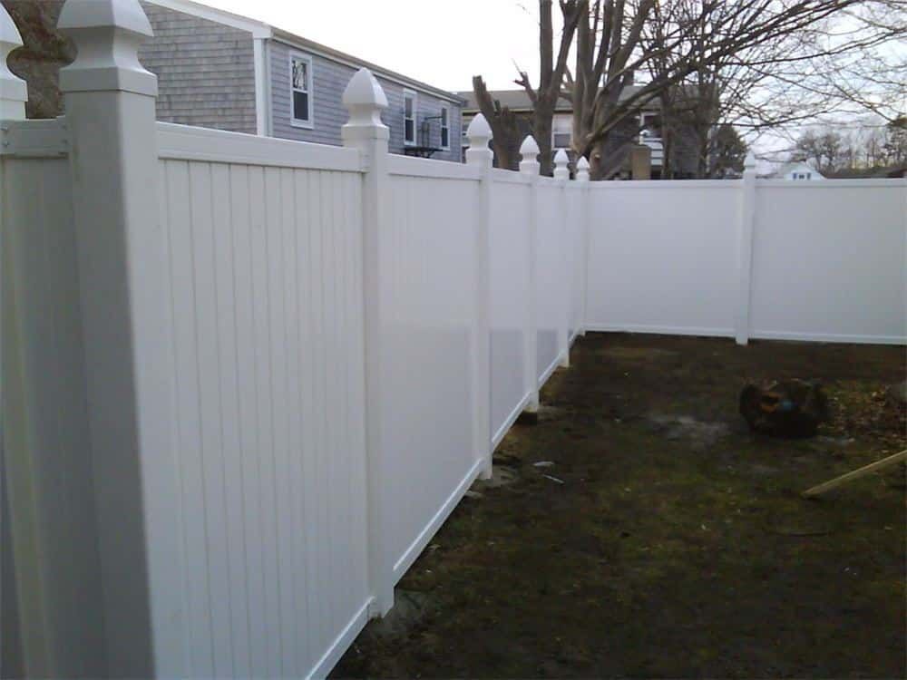 White vinyl fence surrounds a yard, with a building visible in the background.