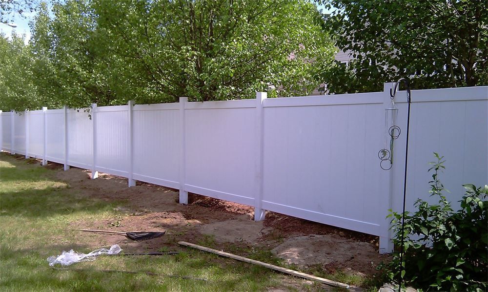 White vinyl privacy fence in a grassy yard, trees in background.