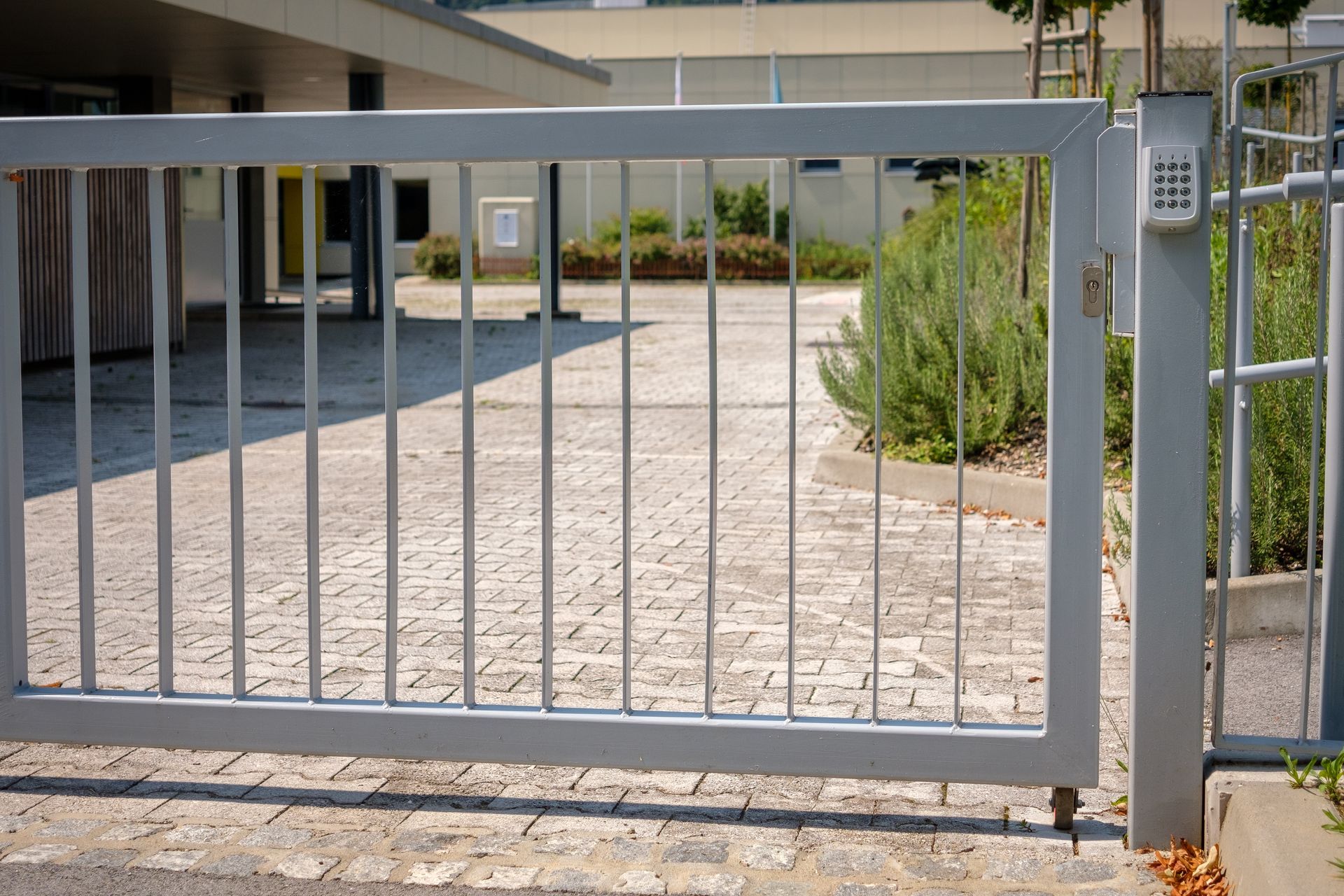 Gray metal gate with keypad, open to a brick paved driveway.