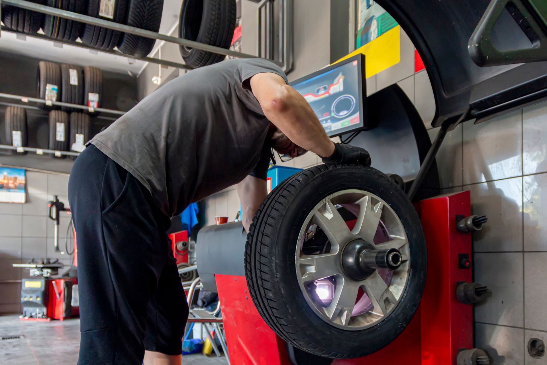 A man is balancing a tire on a machine in a garage.