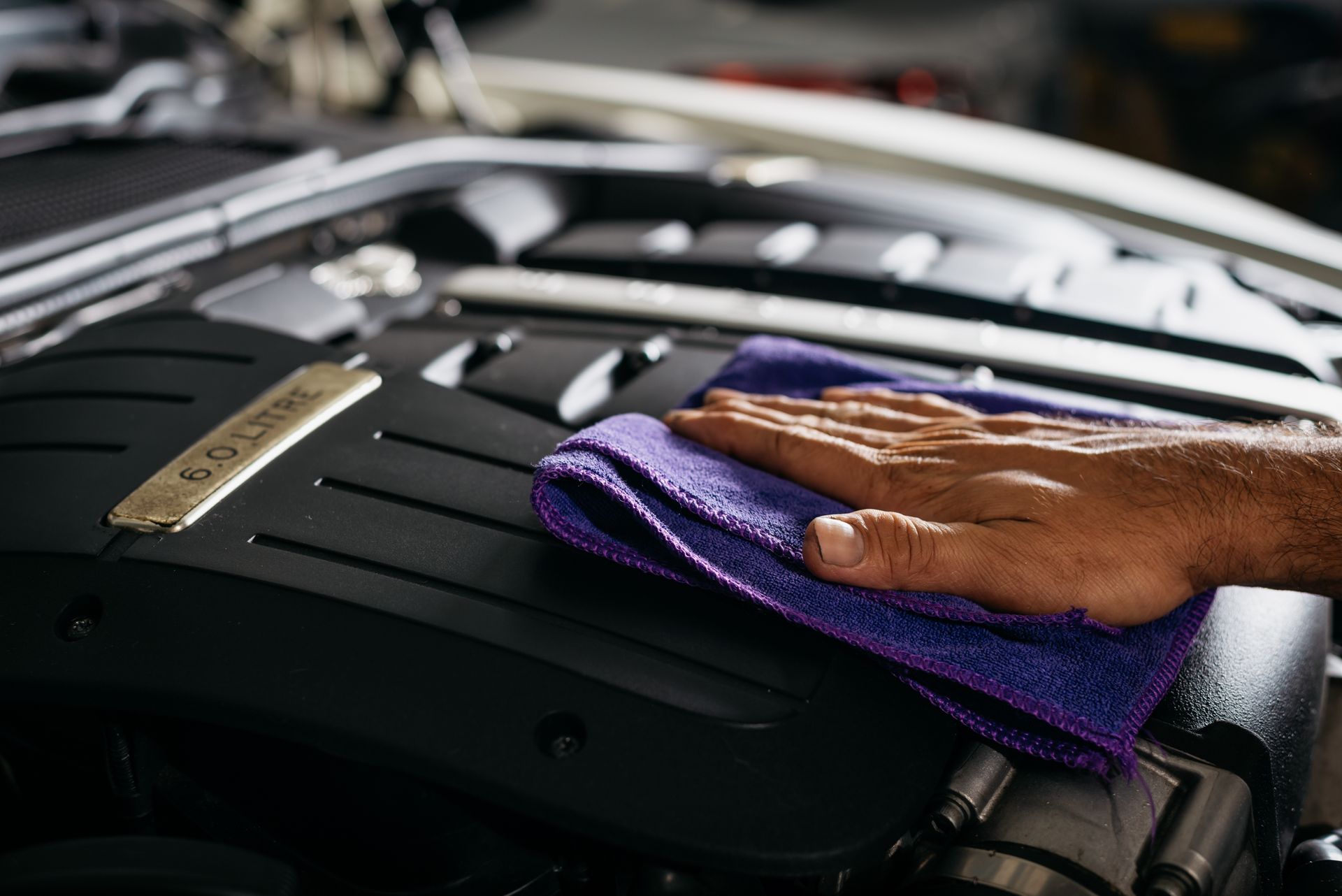 A person is cleaning the engine of a car with a towel.