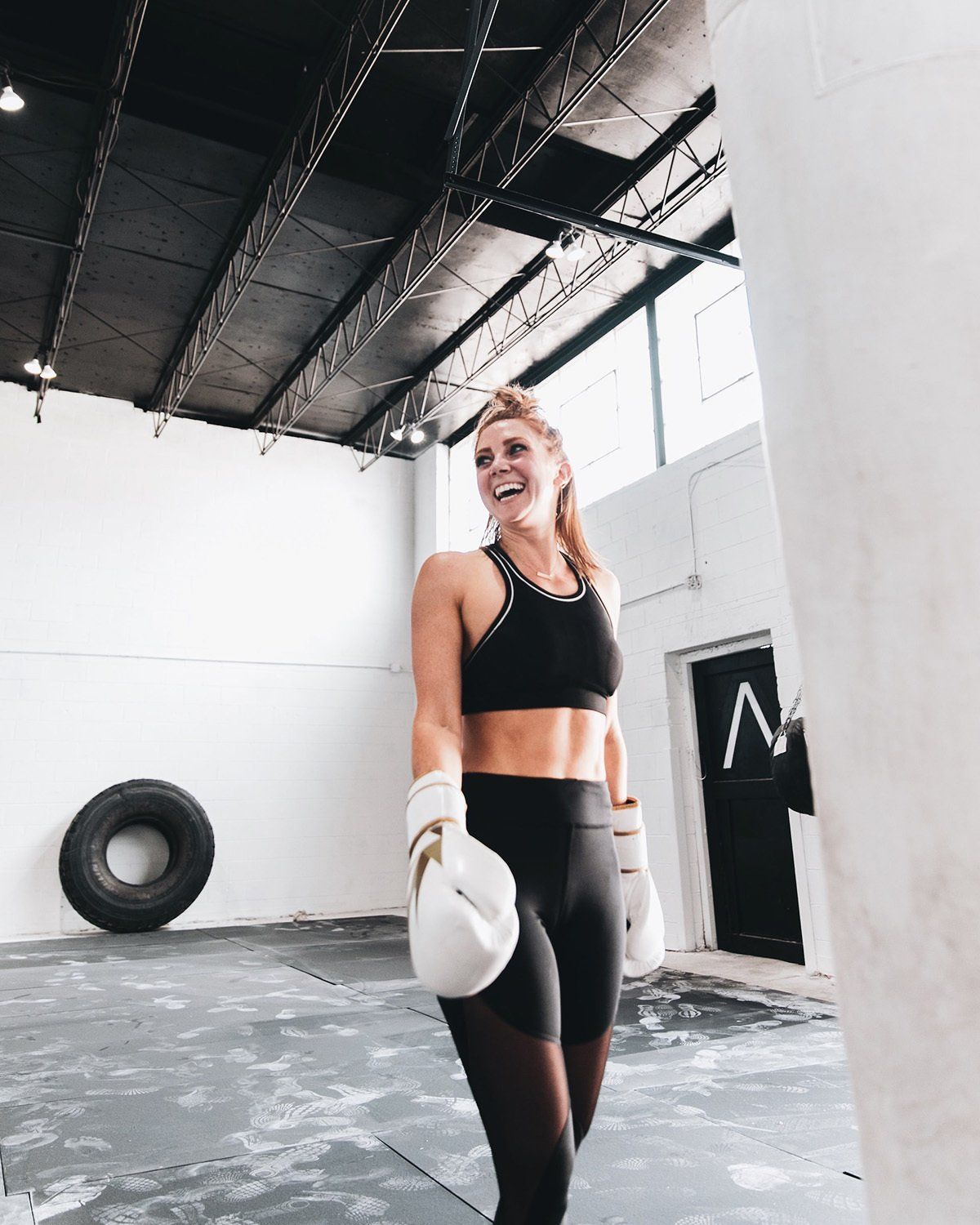 A woman wearing boxing gloves is walking in a gym.