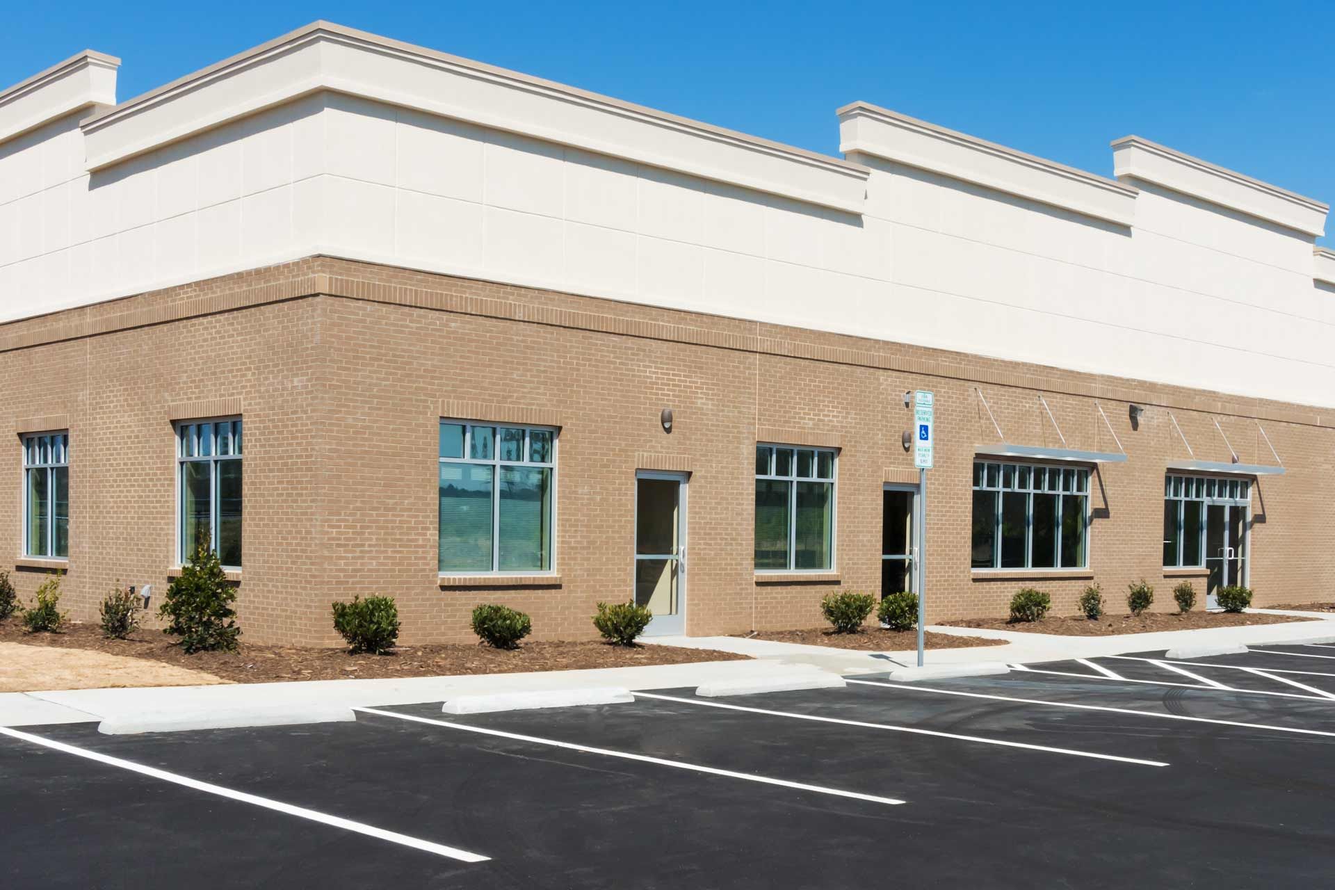 Commercial building exterior with tan brick facade, blue windows, and empty parking lot.