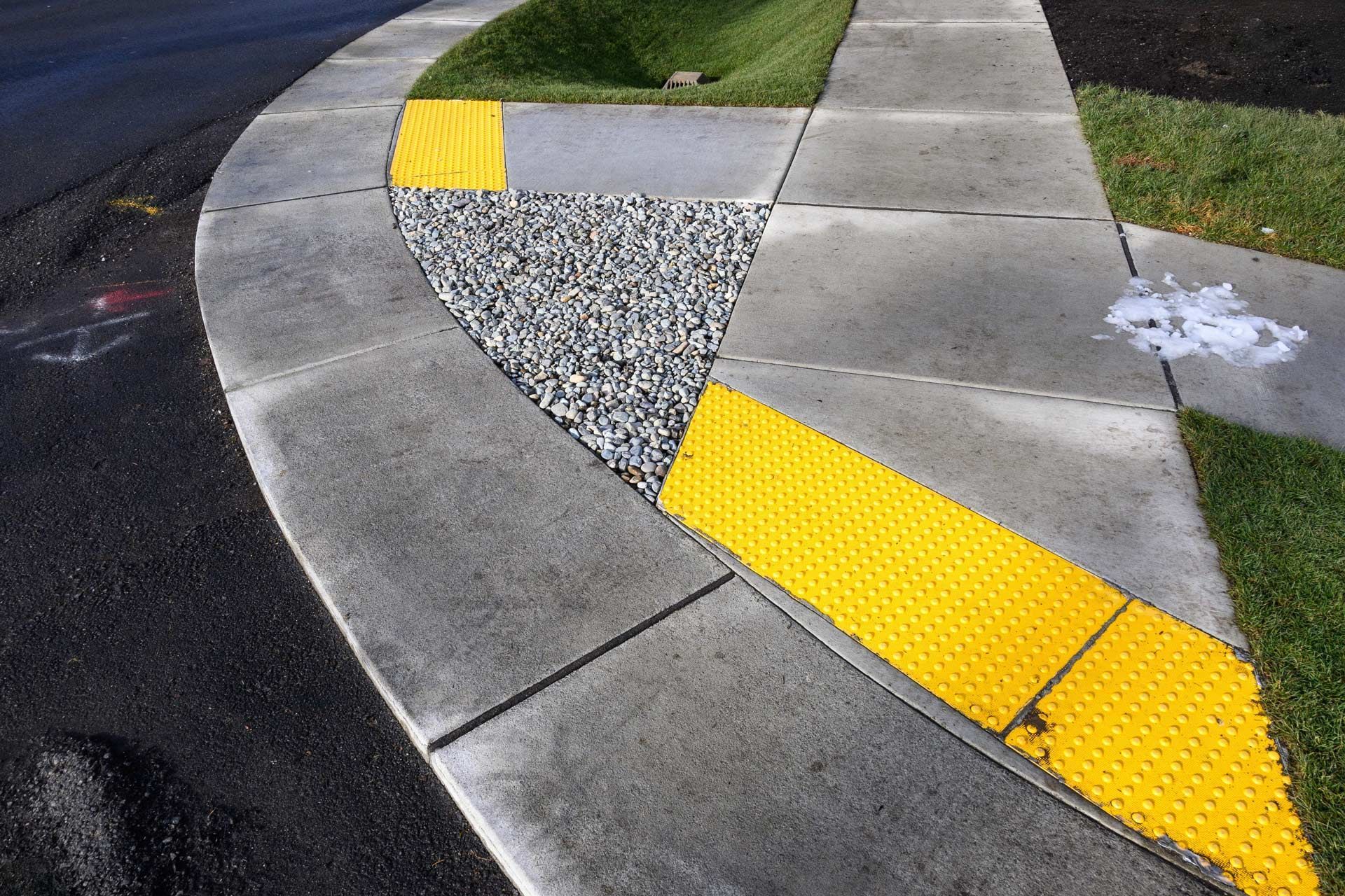 Curbside with yellow tactile paving, a gravel section, and green grass.