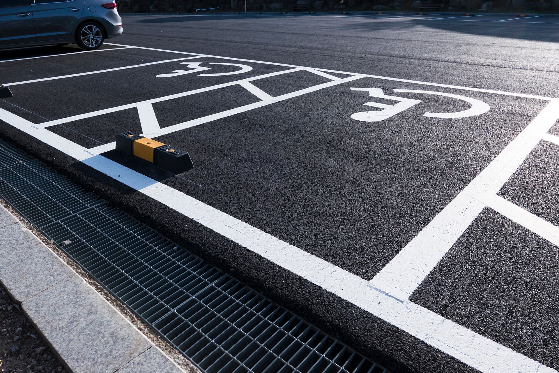 Black asphalt parking space with white markings and a bumper stop for a designated accessible parking area.