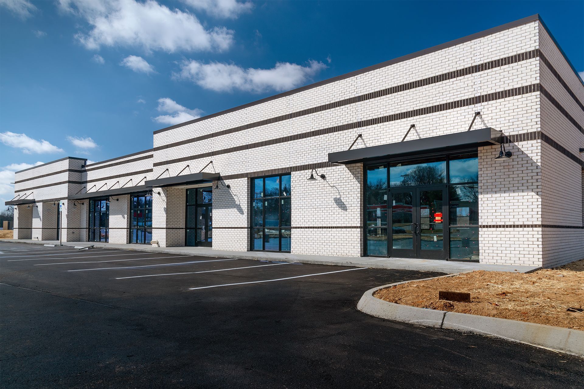 Exterior of a modern building with white brick, black awnings, and large glass windows under a blue sky.