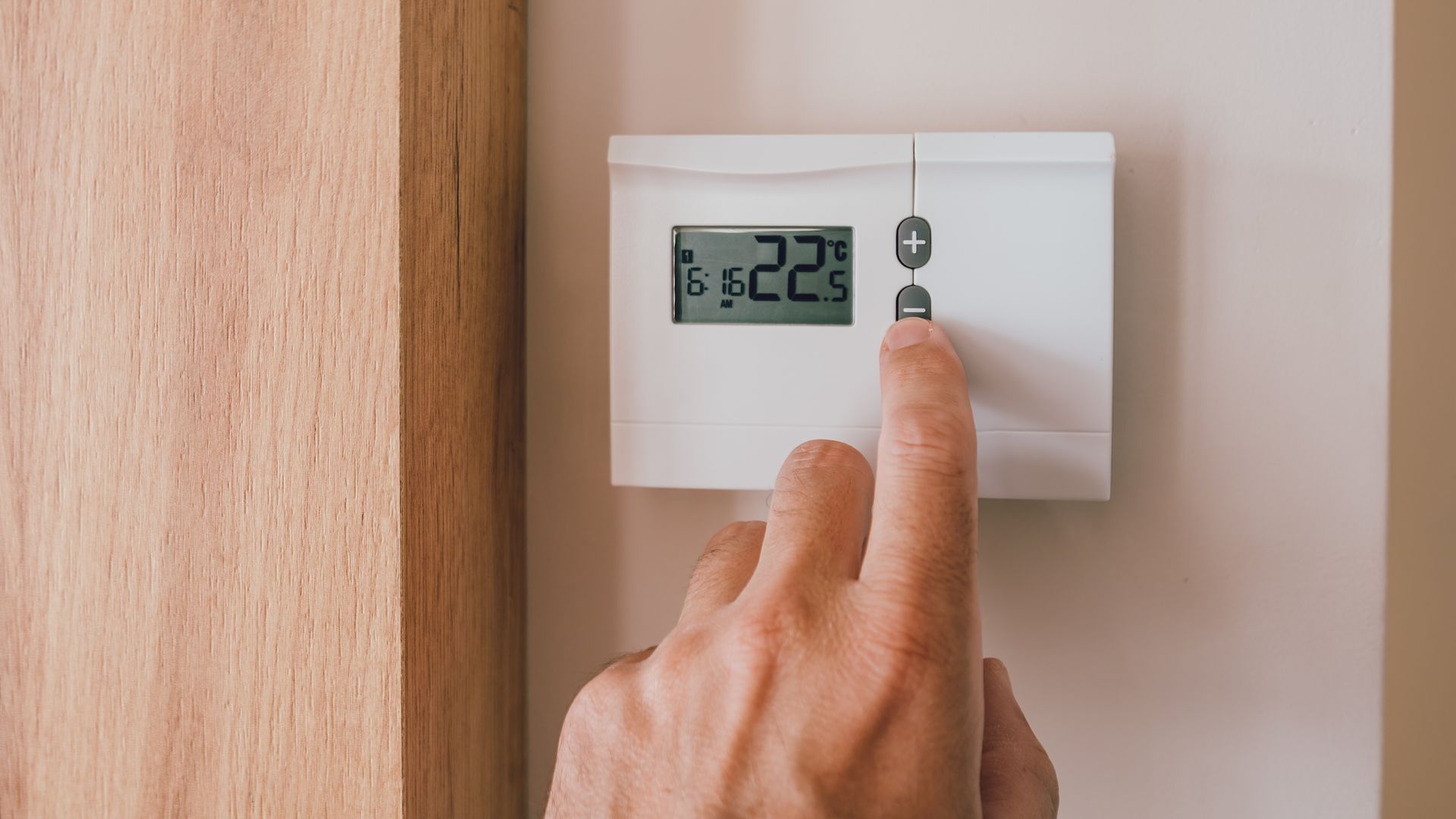 a digital thermostat mounted on a wall next to wooden trim, showing a temperature reading of 22.5°C