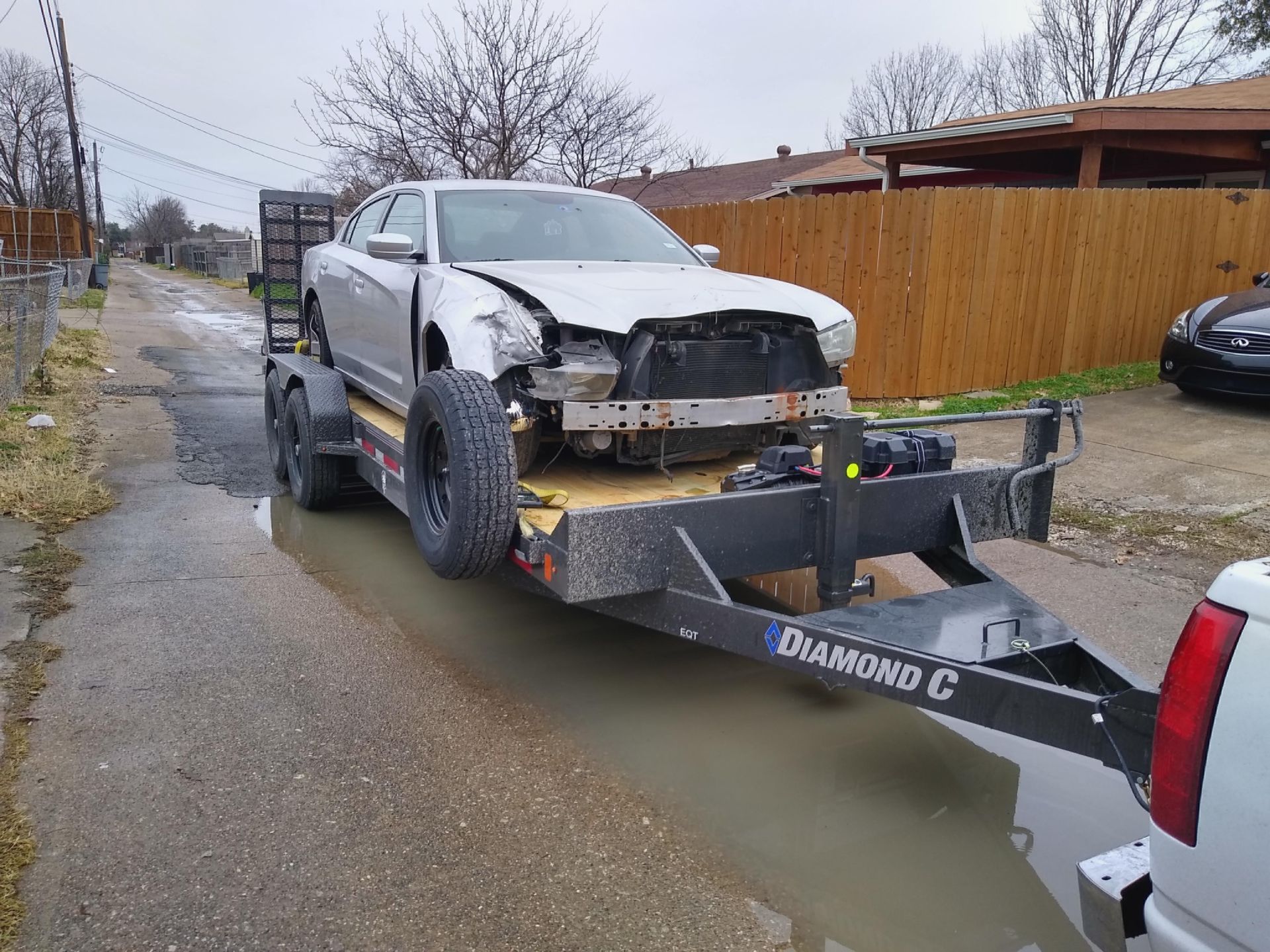 Silver damaged Dodge Charger on a trailer in a residential area.