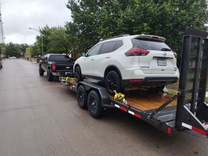 Black truck towing a white SUV on a trailer down a wet street.