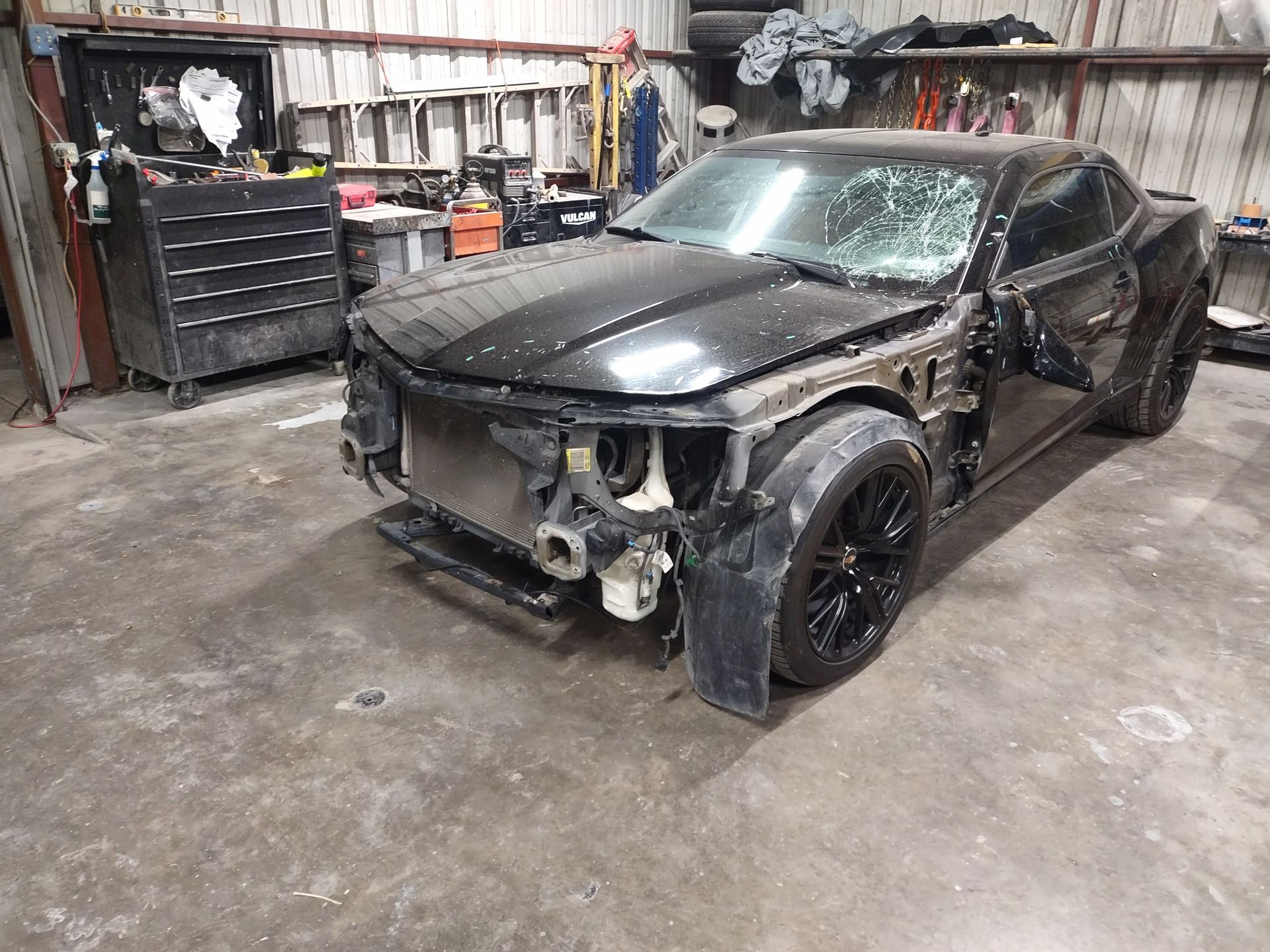 Black car with front end damage in a garage.