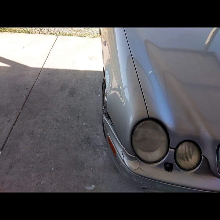 Silver car's front end, partially in shadow, parked on concrete. Headlights visible.