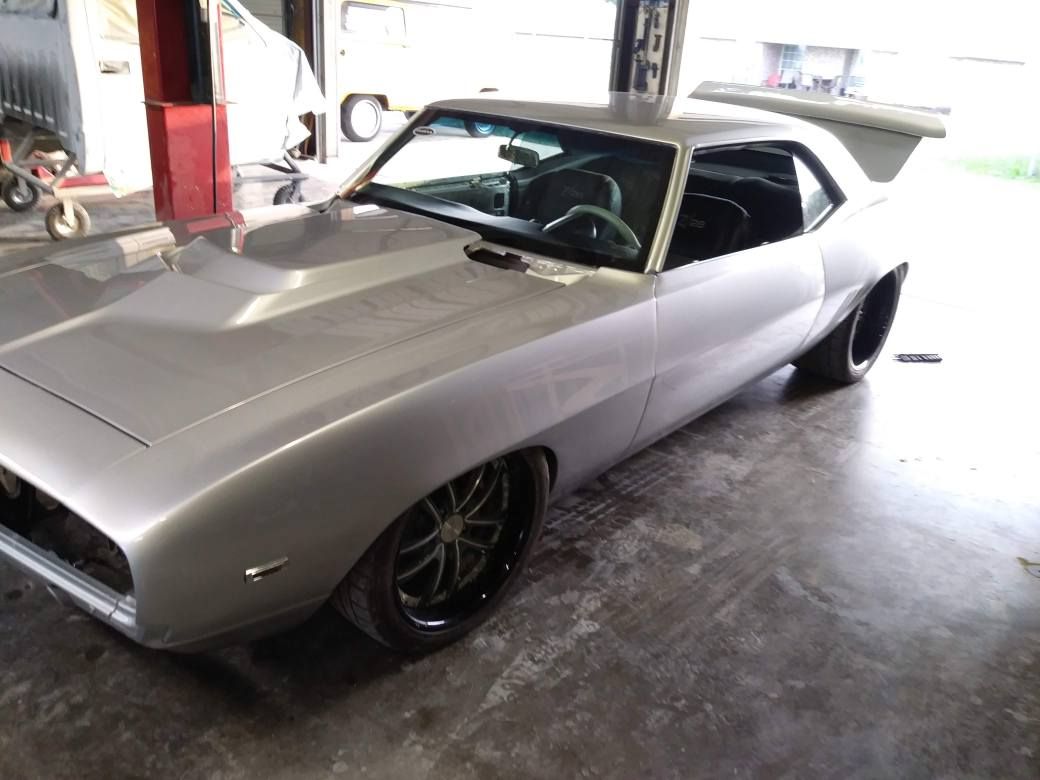 Silver custom 1969 Chevrolet Camaro sports car with a large spoiler, black wheels, in a garage.