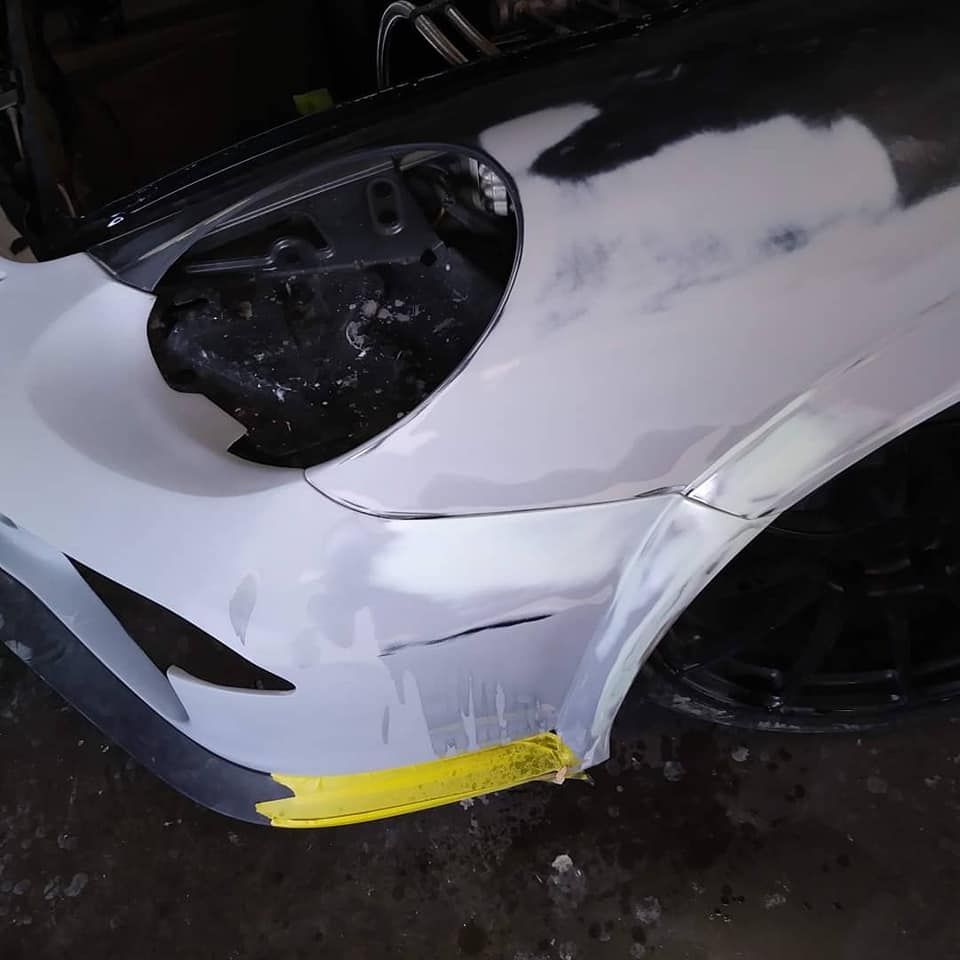 Car bodywork in progress; gray primer on a front fender, with yellow tape and black wheel.
