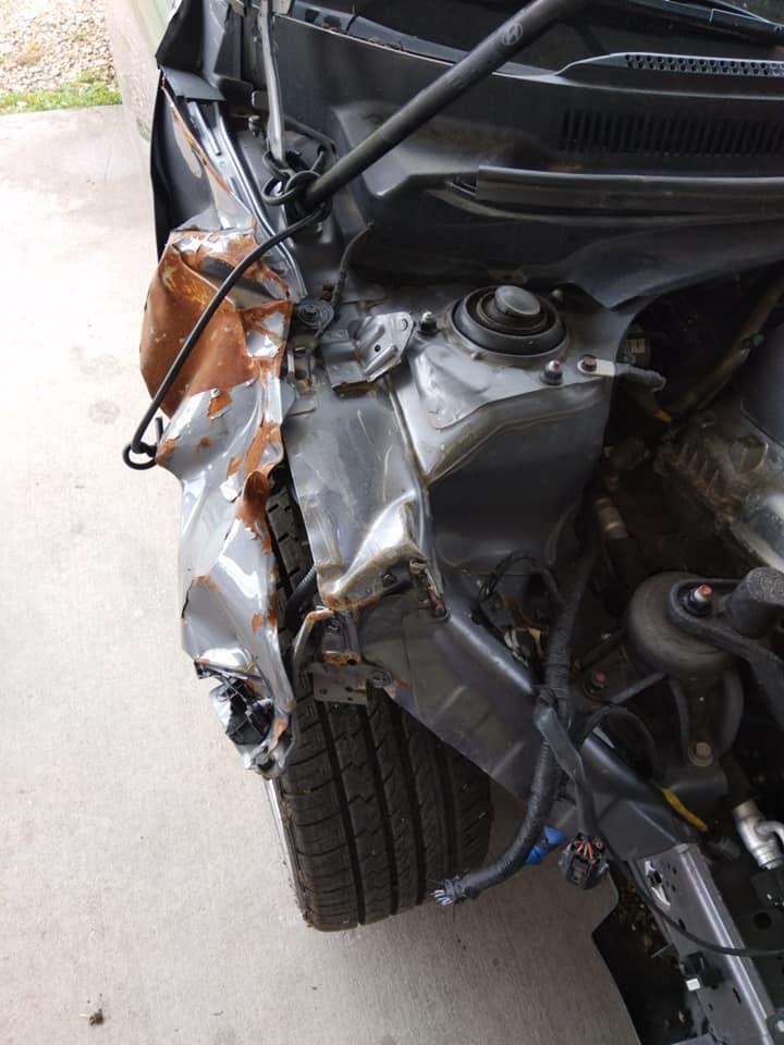 Damaged gray car front-end with crumpled metal and exposed parts, rust visible.