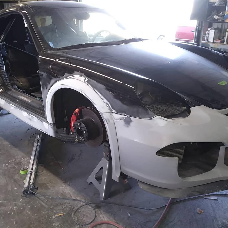 A black Porsche being worked on in a garage, with front fenders removed and body repair underway.