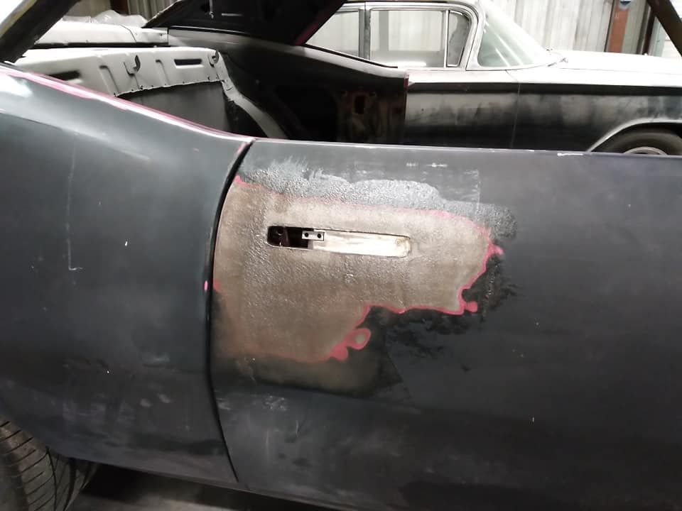 Black car door with bodywork in progress; other classic cars in background.