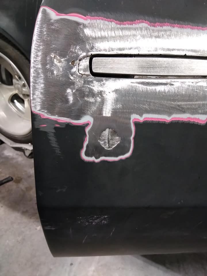 Car door with body work in progress: primer, sanding, and cutouts for the door handle and lock.