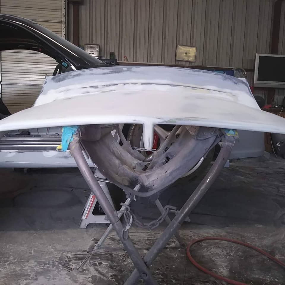 Car hood on stand in a body shop, undergoing repair work; grey paint, metal supports.