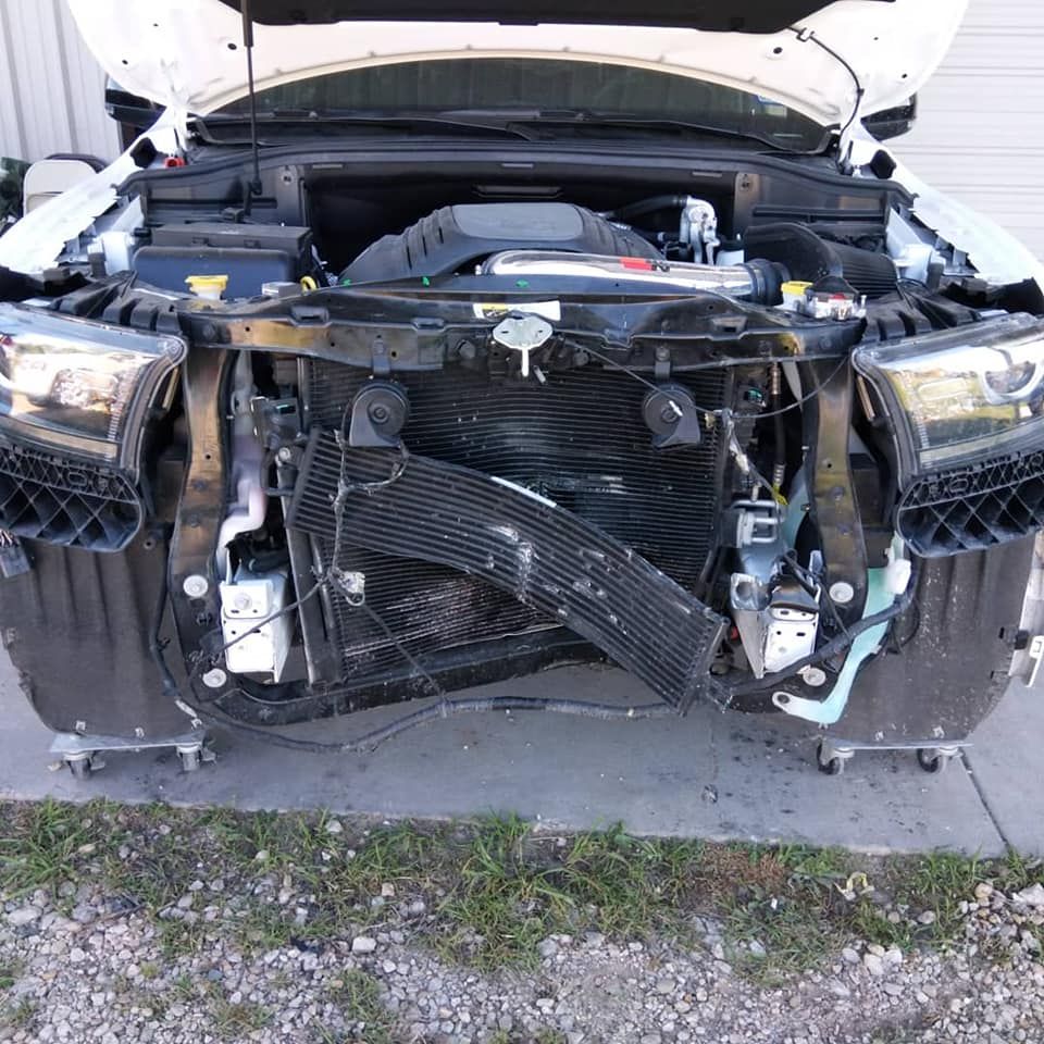 White car with open hood, damaged front end, revealing engine and radiator.