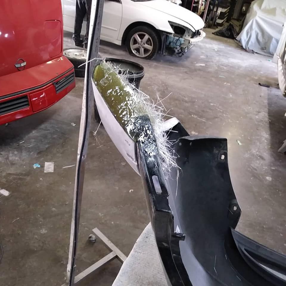 Black car bumper being repaired with fiberglass in a garage.