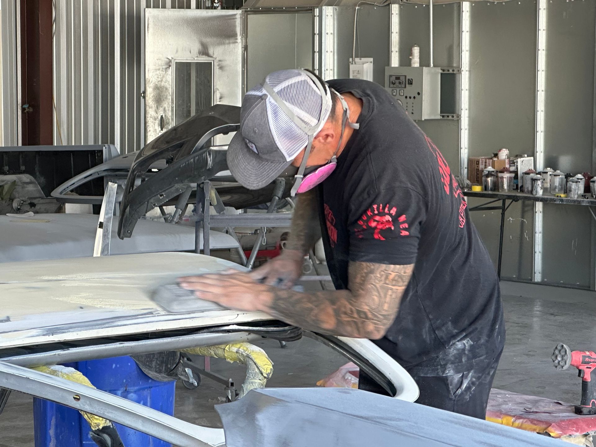 A person wearing a face mask sanding a car roof in a garage.